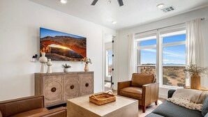 A living room with a large window, a sofa, a coffee table, and a painting on the wall.