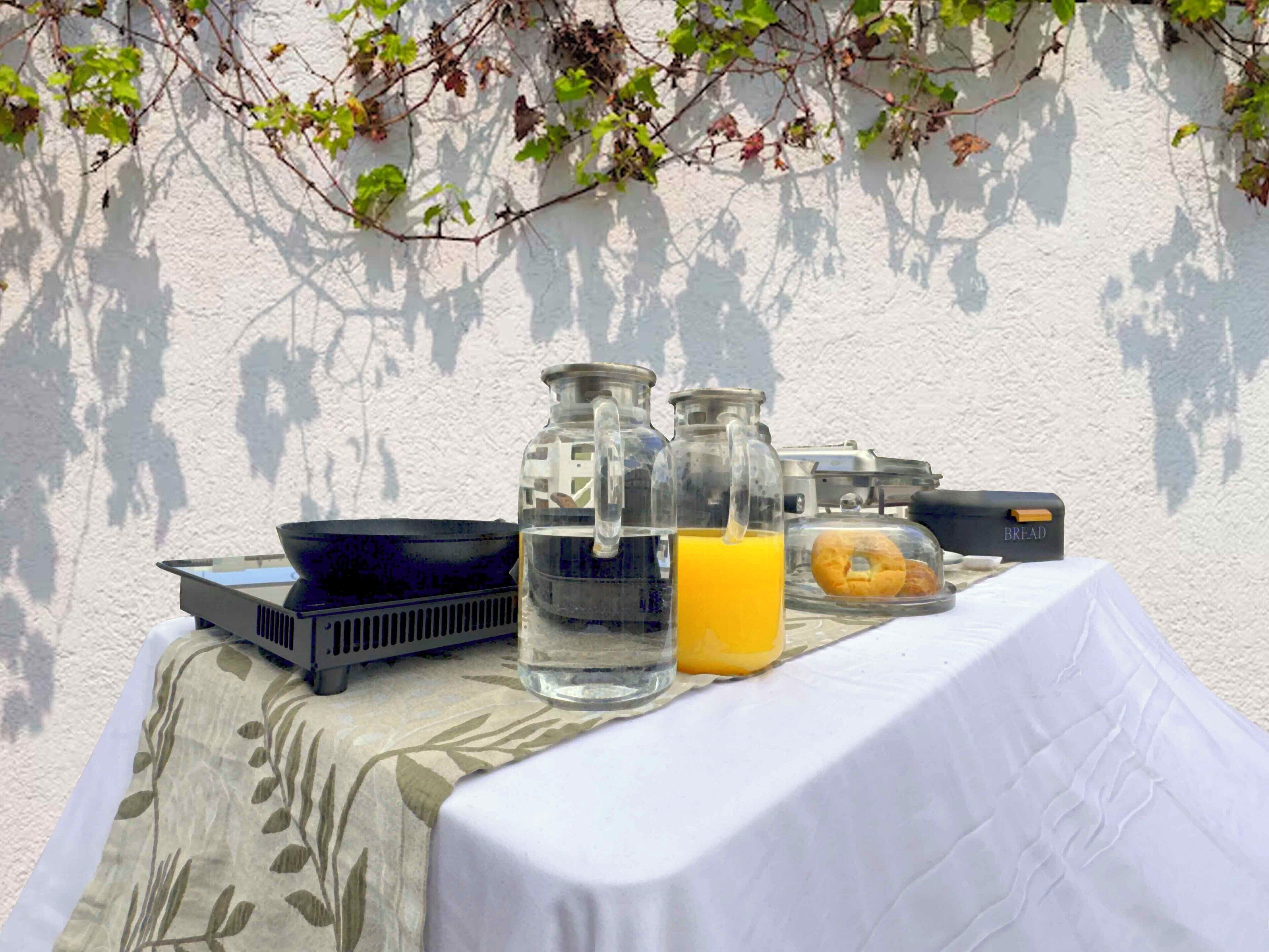 Une table de petit-déjeuner avec une nappe blanche, deux bouteilles en verre, un pichet, un bol et un sac étiqueté « PAIN ».