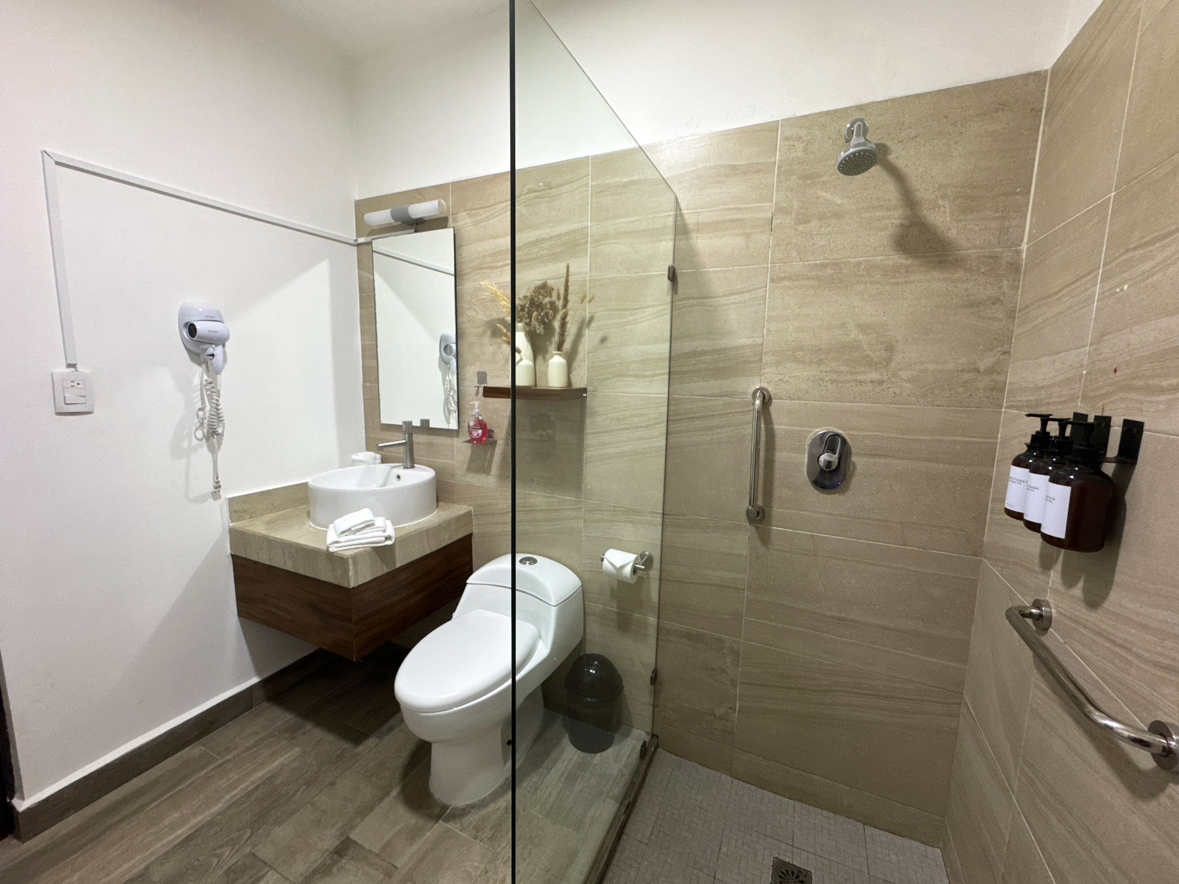 Ein modernes Badezimmer mit Duschkabine aus Glas, Toilette, Waschbecken und einem an der Wand befestigten Föhn.