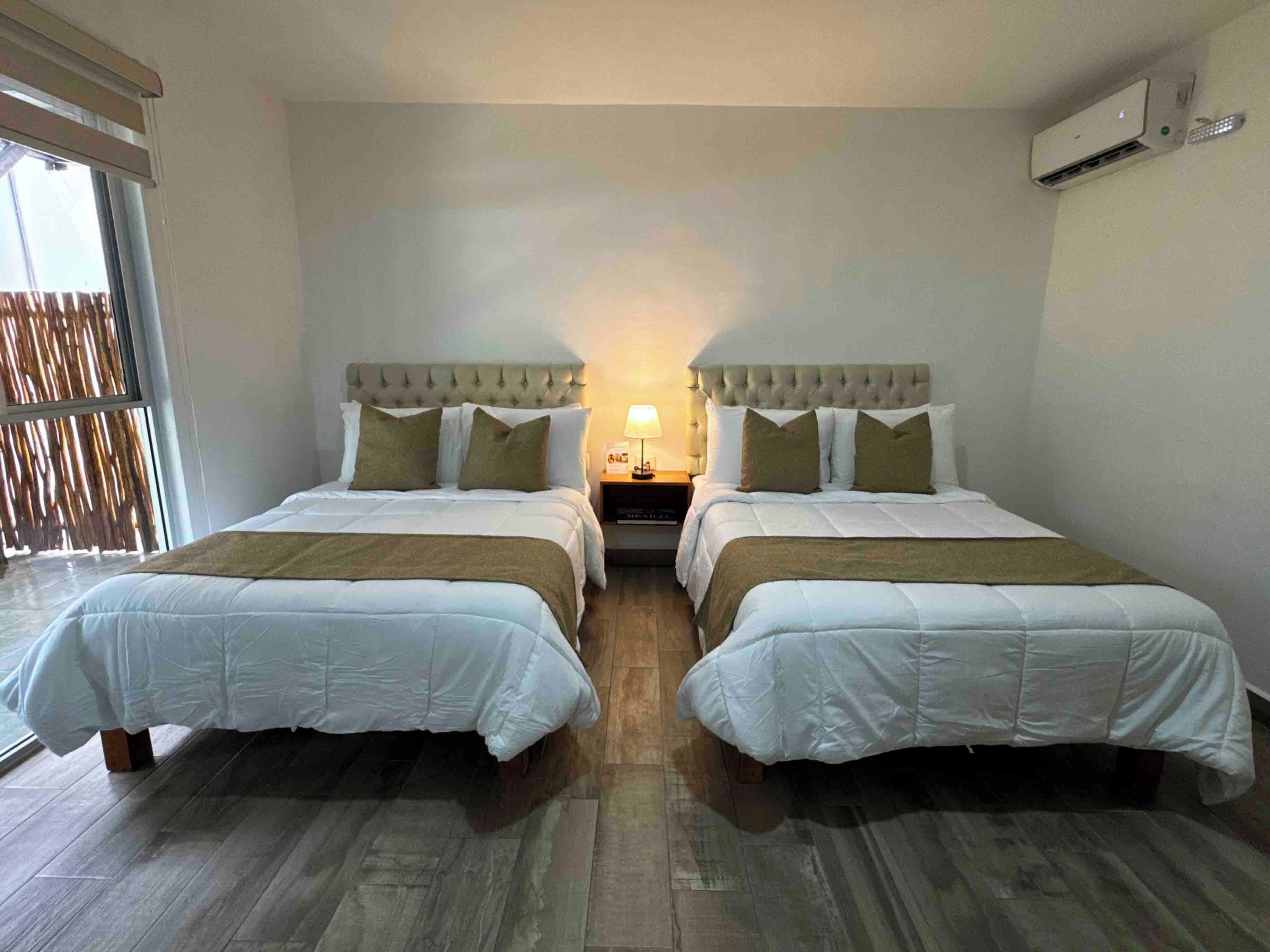 Habitación doble con dos camas, una mesita de noche, una lámpara y un equipo de aire acondicionado.