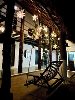 Un columpio con luces en forma de estrella, un banco y un edificio con techo de paja y ventanas grandes.