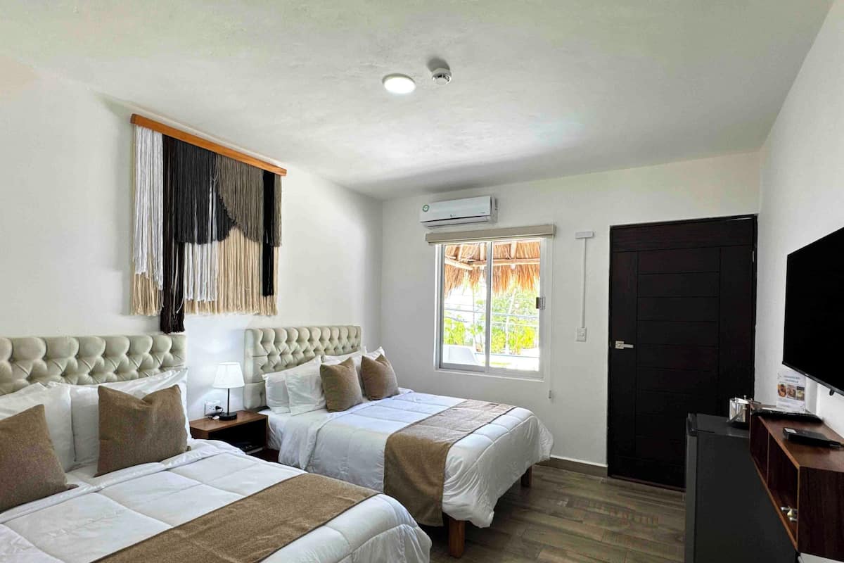 A hotel room with two beds, a TV, a window with a view, and a door.