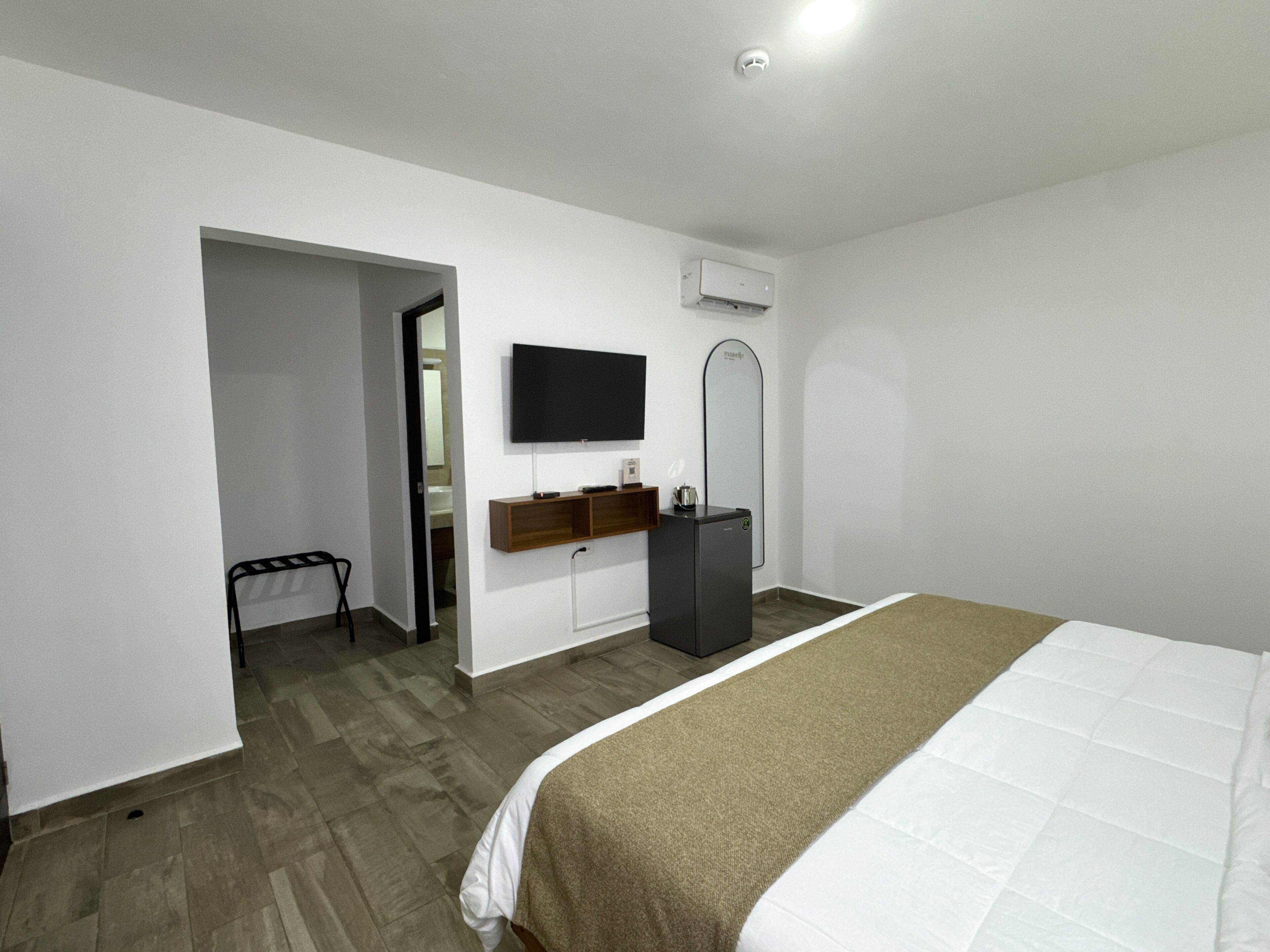A hotel room with a bed, a TV, a mirror, a sink, and a door leading to another room.