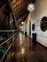 Un pasillo con piso de madera, techo de paja y luces con forma de estrella.