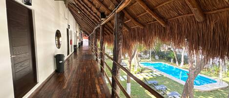 Una terraza cubierta de madera con una piscina al fondo.