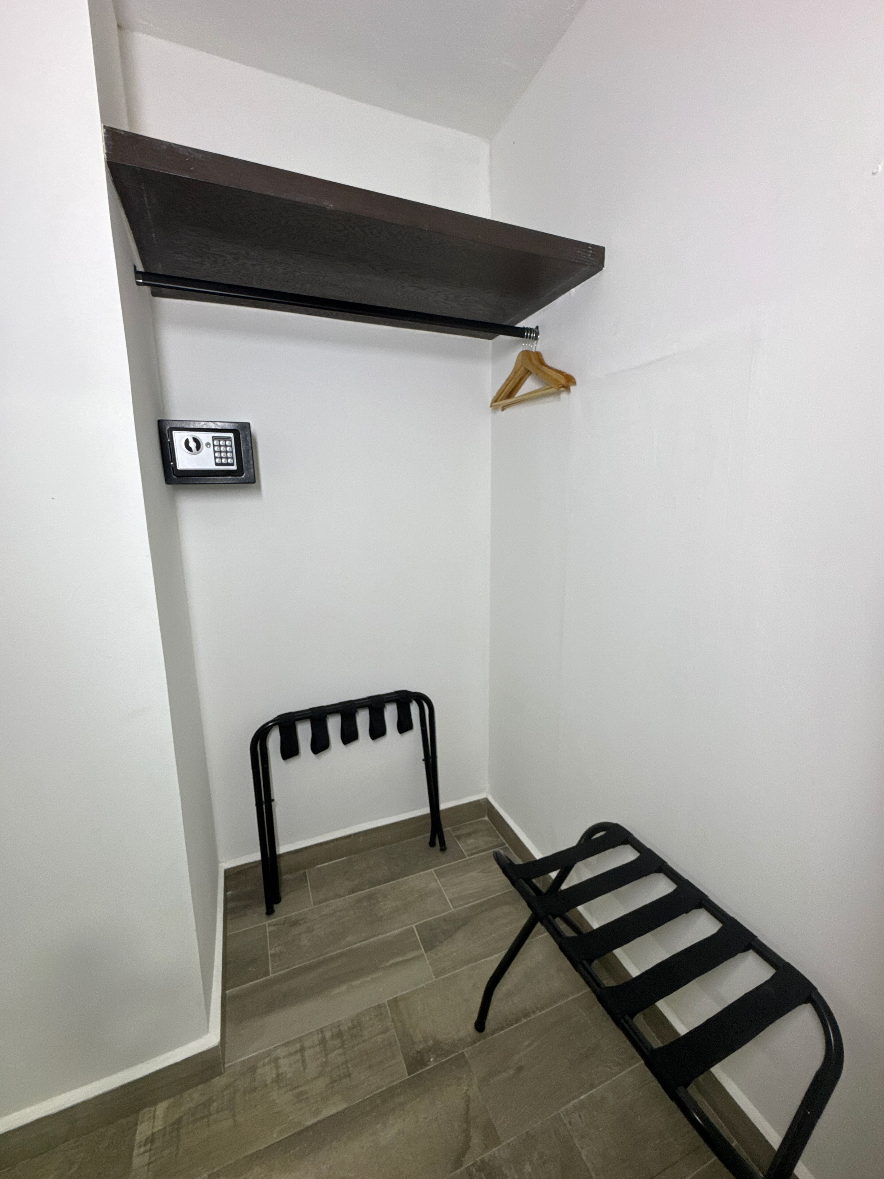 A small room with a black metal bed frame, a wooden hanger, and a wall-mounted electronic lock.