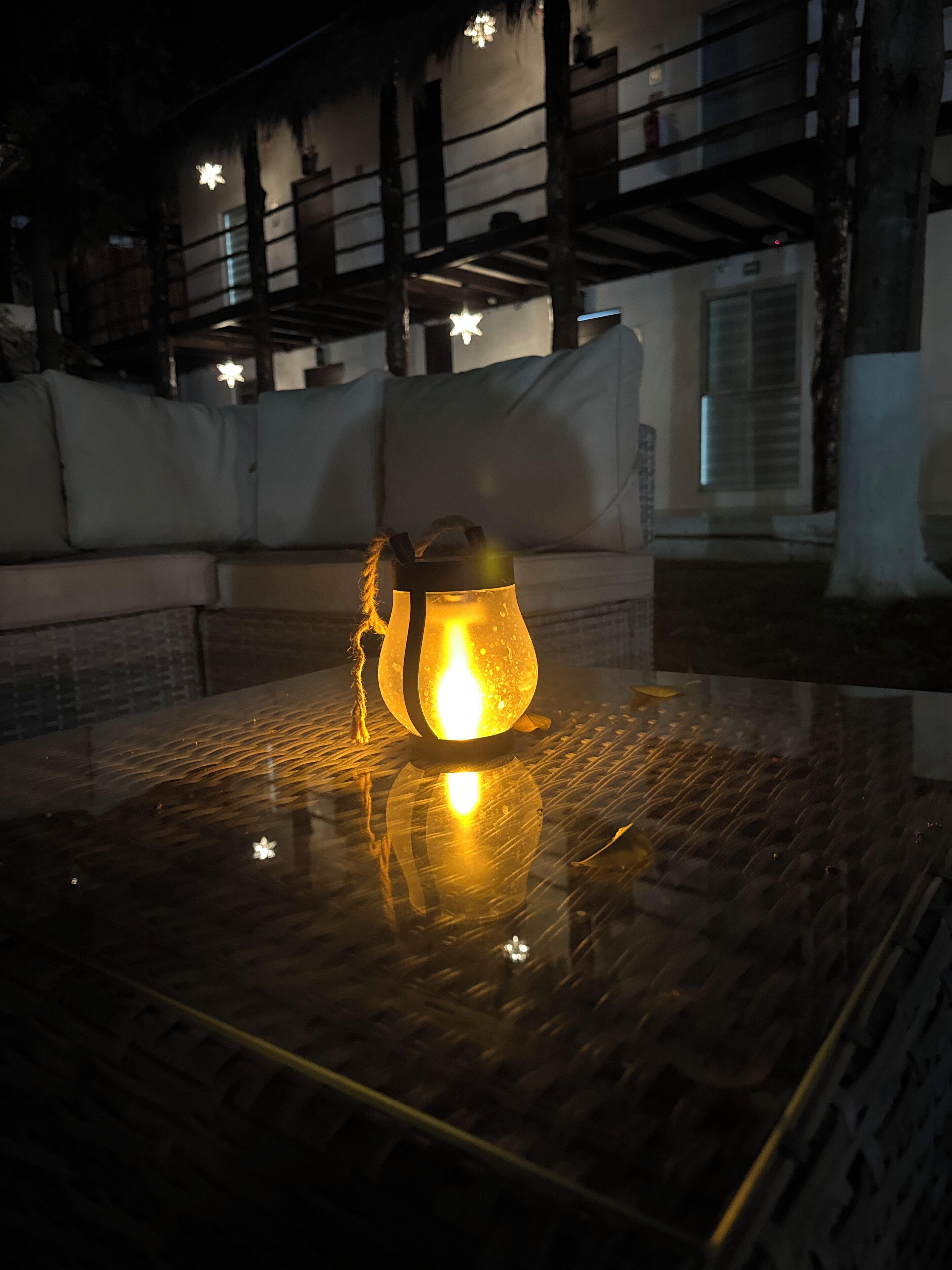 A table with a lit lantern, a sofa, and a railing in the background.