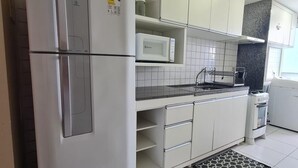 Una cocina moderna con armarios blancos, microondas integrado, refrigerador de acero inoxidable y una alfombra estampada.