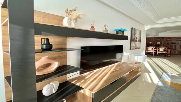Un salon moderne doté d’un grand téléviseur à écran plat, d’étagères en bois et d’une table basse.