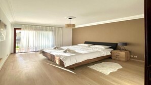 Une chambre avec un grand lit, un plancher en bois, une table de chevet et une vue sur l’extérieur.