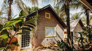 Una casa rústica con fachada de ladrillo y detalles en amarillo, rodeada de exuberante vegetación tropical.
