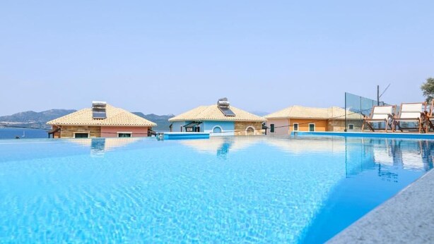Una piscina a sfioro di colore blu intenso con tre ville sulla spiaggia, ciascuna con tetto in tegole e un piccolo balcone.