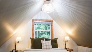 Una habitación acogedora con forma triangular, una cama, dos mesitas de noche y una ventana.