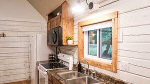 Cocina compacta con paredes de madera blanca, encimera de granito, pileta de acero inoxidable y ventana con vista a la vegetación.