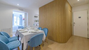 Ein Essbereich mit einem weißen Tisch, gedeckt für sechs Personen, blauen Stühlen und einer Wand als Holzdekor.
