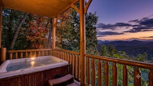 Une terrasse en bois avec un jacuzzi et un banc en bois, offrant une vue sur un paysage montagneux.