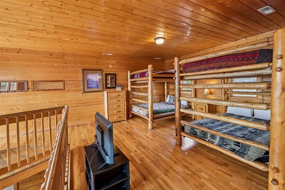 A wooden cabin interior with bunk beds, a television, and a fireplace.