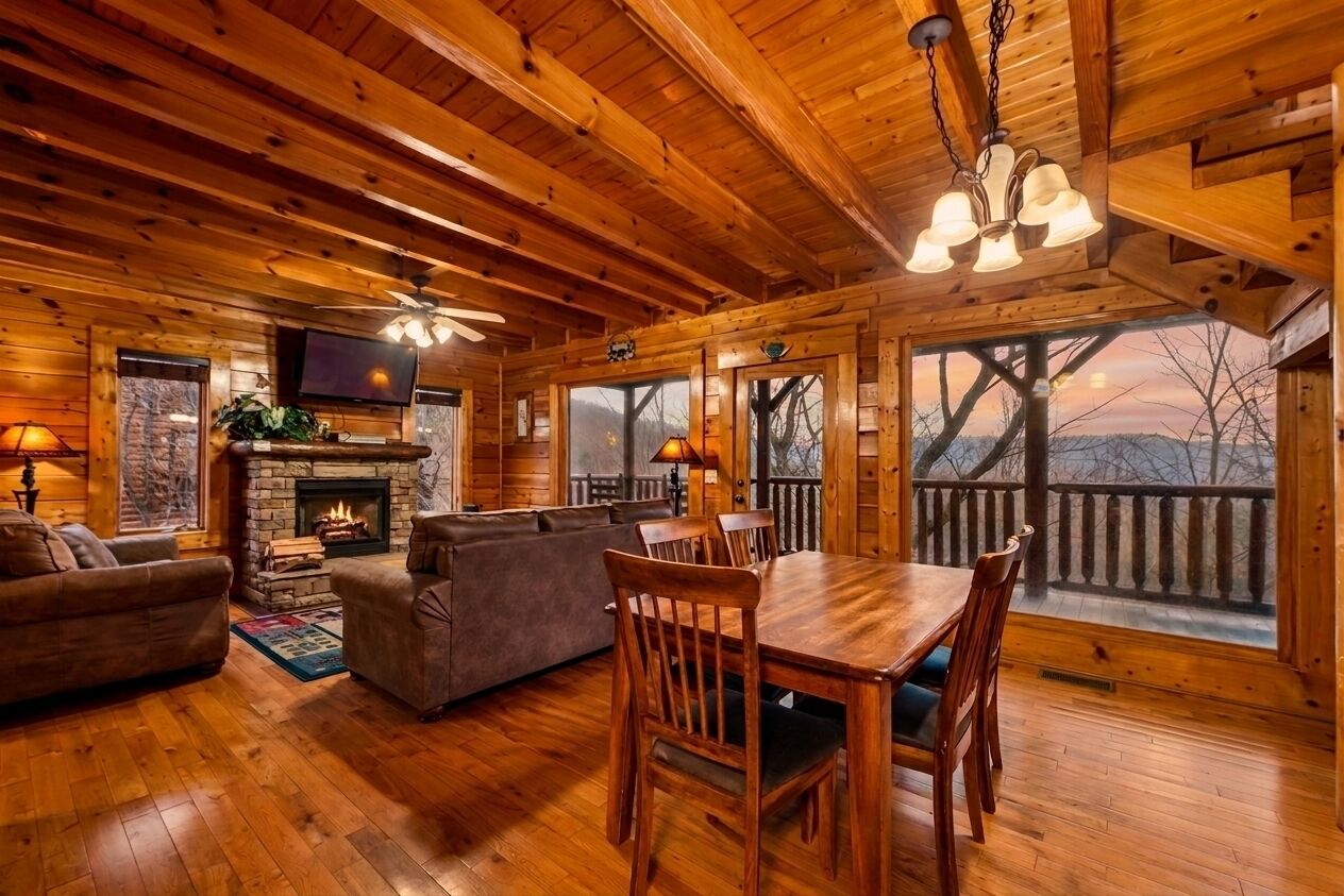 L’intérieur d’un chalet en bois comprend une cheminée, un coin salon, une table à manger et de grandes fenêtres donnant sur l’extérieur.