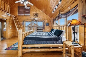 Una habitación tipo cabaña de madera con una cama de madera, un escritorio y un ventilador de techo.