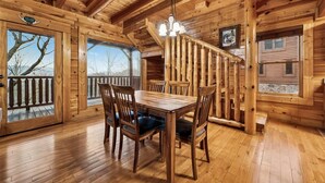 Ein Holzhütten-Interieur mit Esstisch, Stühlen, einer Treppe und großen Fenstern.