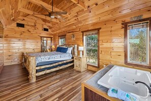 Dormitorio de cabaña de madera con una cama, una mesita de noche de madera, una ventana y un baño con bañera.