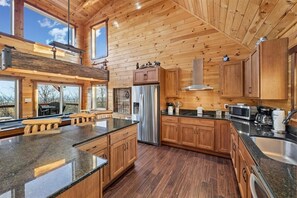 A spacious kitchen with wooden cabinets, a stainless steel refrigerator, and a large island. - Spacious Cabin with Year-Round Mountain Vistas (Sevierville)