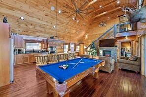 Un interior de madera con mesa de billar, una escalera y una chimenea.