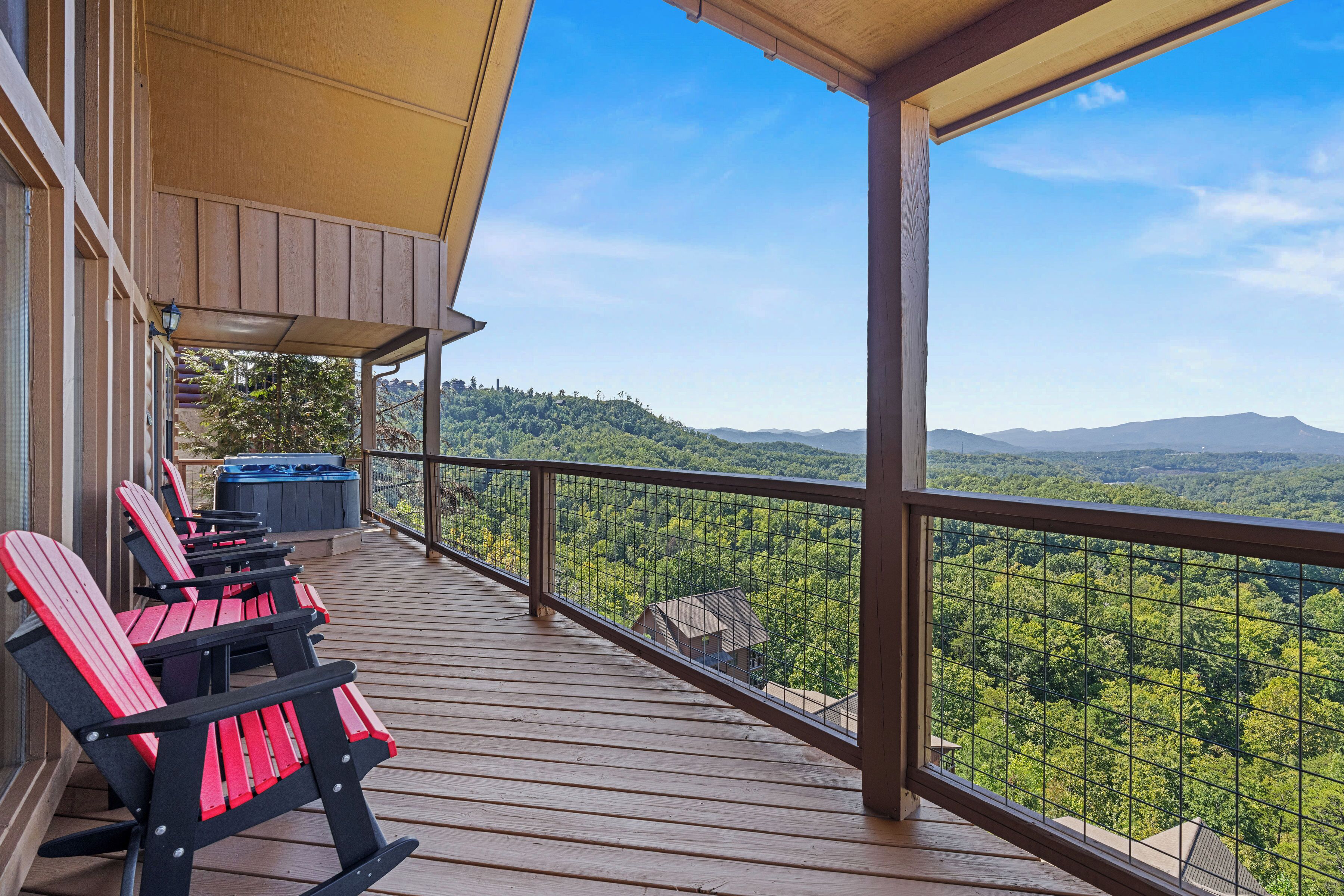 A wooden deck with Adirondack chairs and a hot tub, overlooking a forested landscape.