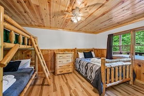 Een houten slaapkamer met een stapelbed, een enkel bed, een dressoir en een plafondventilator.