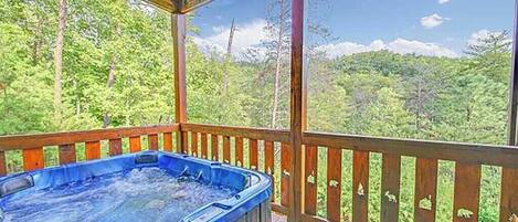 Un jacuzzi en una terraza de madera con vistas a un paisaje boscoso.