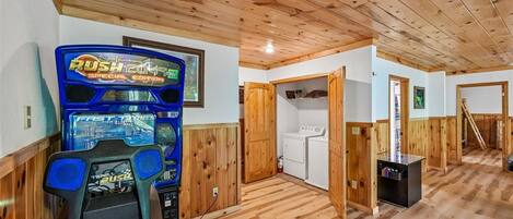 Una habitación con piso de madera, lavadora y una máquina arcade azul.