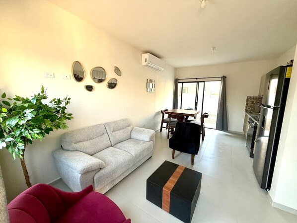 A living room with a sofa, a coffee table, and a dining area with a table and chairs. - Cozy Modern Retreat with Pool (La Paz)