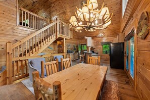 A wooden cabin interior with a dining table, chairs, a staircase, and a chandelier. - Lakefront Cabin w/ Theater & Game Room (Sevierville)