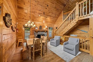 A wooden cabin interior with a dining area, two armchairs, a fireplace, and a staircase. - Lakefront Cabin w/ Theater & Game Room (Sevierville)