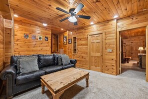 A log cabin interior with a leather sofa, a wooden coffee table, a ceiling fan, and wooden walls. - Lakefront Cabin w/ Theater & Game Room (Sevierville)