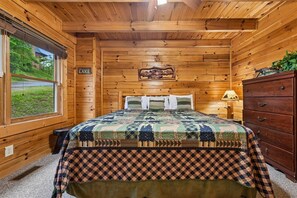 A wooden cabin bedroom with a bed, dresser, and a window with a view of a lake. - Lakefront Cabin w/ Theater & Game Room (Sevierville)