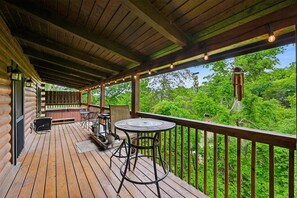 Eine Holzterrasse mit Tisch und Stühlen, einem Whirlpool und Blick auf ein bewaldetes Gebiet.