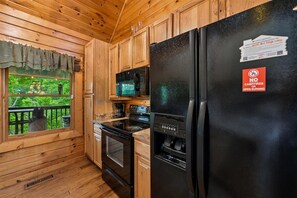 A cabin kitchen with wooden cabinets, a black refrigerator, a microwave, and a stove. - Lakefront Cabin w/ Theater & Game Room (Sevierville)