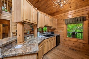 A wooden cabin interior with a kitchen area, granite countertops, and a window overlooking a deck. - Lakefront Cabin w/ Theater & Game Room (Sevierville)