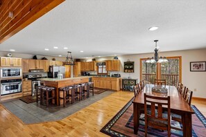 A spacious kitchen with wooden cabinets, a central island, bar stools, and a dining area with a long table and chairs. - 6‑Bedroom Mountain Escape with Forested Views (Sevierville)