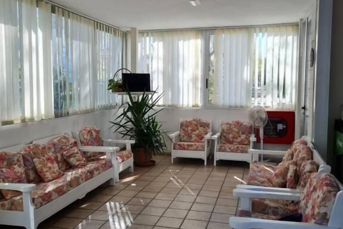 Een ruime kamer met een witte zithoek, twee fauteuils, een kleine tafel en een potplant.