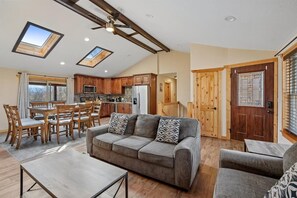 A spacious living area with a sofa, dining table, and chairs, a kitchen with wooden cabinets, and skylights. - Relax & Unwind w/ Hot Tub & Games (Sevierville)