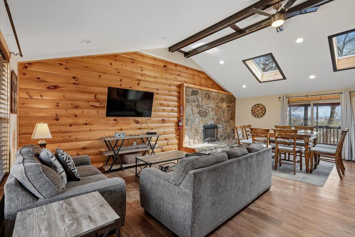 A log cabin interior with a fireplace, wooden walls, a television, and a dining area.