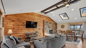 L’intérieur d’une cabane en rondins, avec une cheminée, des murs en bois, un téléviseur et un coin repas.