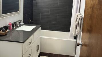 A modern bathroom with a bathtub, a shower, a sink with a mirror, and a toilet.
