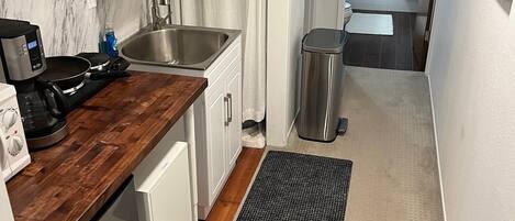 Una cocina compacta con encimera de madera, un lavamanos de acero inoxidable y un pequeño cubo de basura.