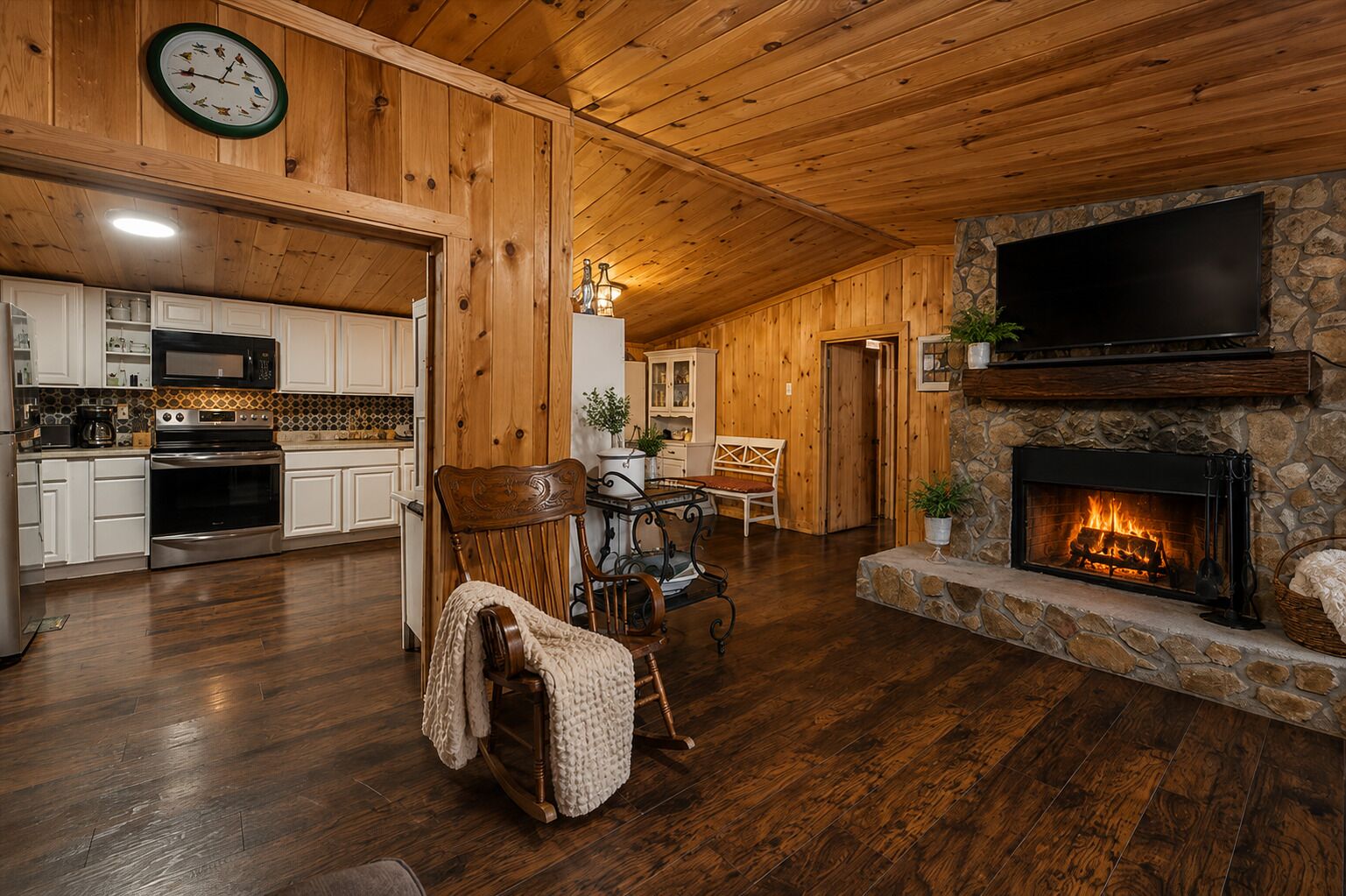 A cozy interior with a stone fireplace, wooden ceiling, and a kitchen area with modern appliances.