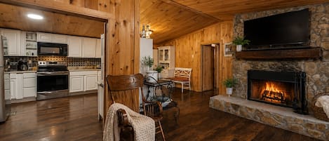 A cozy interior with a stone fireplace, wooden ceiling, and a kitchen area with modern appliances.