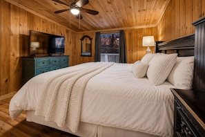 A wooden-paneled bedroom with a bed, a television, a dresser, and a window with a view. - Charming Mountain Hideaway w/ Hot Tub (Sevierville)