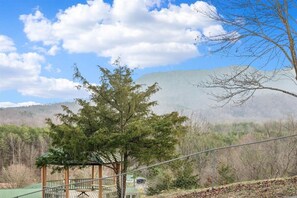 A gazebo with a metal railing, surrounded by trees and a mountainous backdrop.